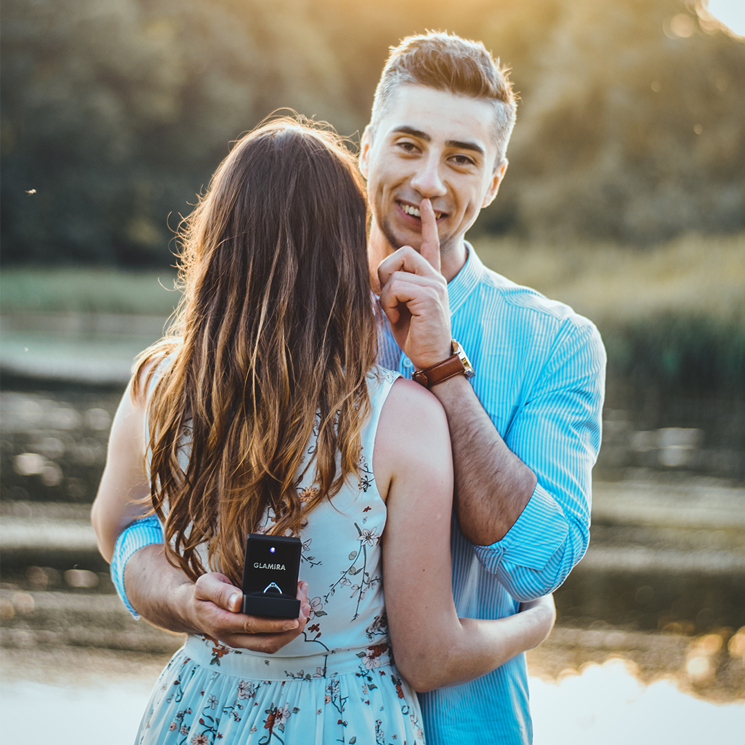 man holding engagement ring behind brides back